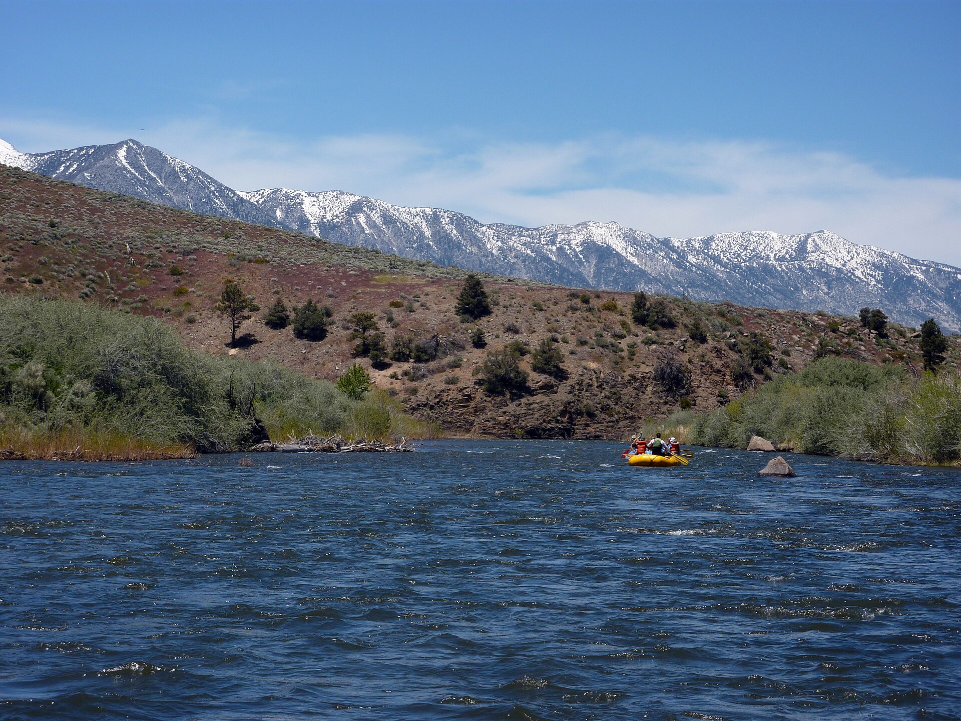 A raft floats on the East Fork Carson River below snow-covered Sierra Nevada slopes.